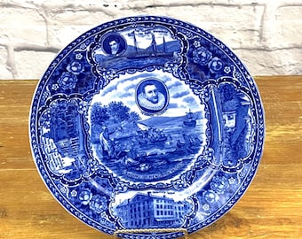 Puede incluir: Plato de cerámica azul y blanco con un diseño decorativo que representa una escena del desembarco de Hendrick Hudson. El plato tiene un borde floral azul y blanco e incluye el texto "Landing of Hendrick Hudson".
