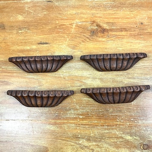 Puede incluir: Cuatro tiradores de cajón de madera marrón con un borde festoneado y un diseño de madera tallada.