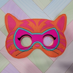 May include: An orange felt cat mask featuring pink tiger stripes, a bright pink eye mask area outlined in teal, and black embroidered whiskers and eyelashes. The mask has two circular eye cutouts and is constructed with visible stitching.