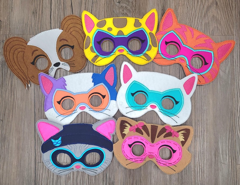 May include: A collection of seven felt animal masks featuring various designs including a brown and white dog, a yellow leopard, an orange tabby cat, a white cat with a blue mask, a grey cat with a beanie, and a brown cat with pink accents.