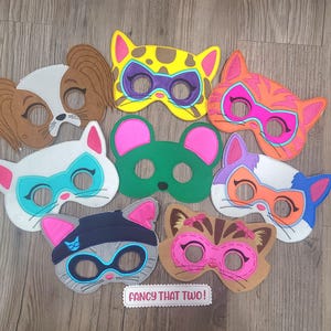 May include: A collection of eight felt animal masks featuring various designs including a brown dog, a yellow cat, an orange cat, a white cat, a green mouse, a multi-coloured cat, a grey cat, and a brown cat. A white label reads FANCY THAT TWO!