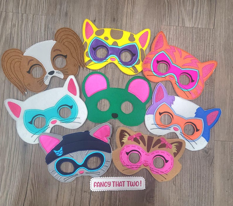 May include: A collection of eight felt animal masks featuring various designs including a brown dog, a yellow cat, an orange cat, a white cat, a green mouse, a multi-coloured cat, a grey cat, and a brown cat. A white label reads FANCY THAT TWO!