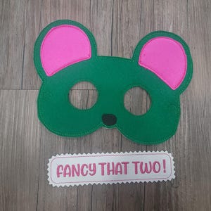 May include: A green felt animal mask with bright pink inner ears and a small black nose. Below the mask is a white rectangular felt patch with pink scalloped edges featuring the embroidered pink text "FANCY THAT TWO!" in a bold font.