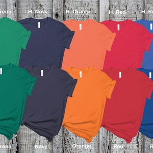 May include: Ten blank t-shirts in various colors, including kelly green, navy, orange, red, and royal blue. The shirts are laid out on a wooden surface.