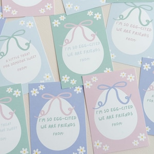 K&ouml;nnte beinhalten: Ein Satz druckbarer Ostergeschenkanh&auml;nger mit einem Cartoon-Ei mit Schleife. Die Anh&auml;nger haben verschiedene Botschaften, darunter "Some bunny loves you" und "I'm so egg-cited we are friends".