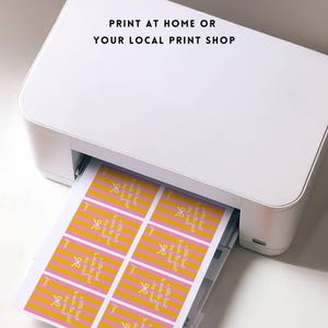 Pu&ograve; includere: Una stampante bianca che stampa fogli di etichette con un design a righe rosa e gialle. Le etichette hanno testo e una grafica a fiocco. Il testo sull'immagine recita "PRINT AT HOME OR YOUR LOCAL PRINT SHOP."