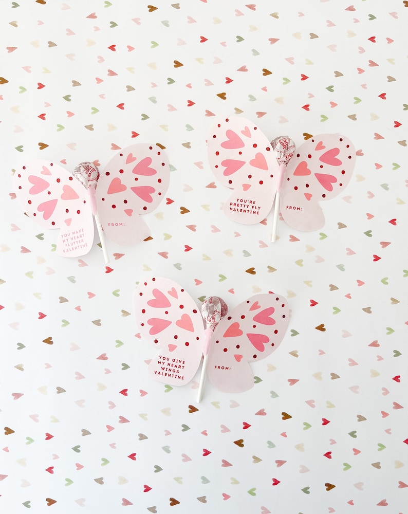 May include: Three pink butterfly-shaped Valentine's Day cards with lollipop sticks. Each card has a different message: "You have my heart flutter Valentine", "You're pretty fly Valentine", and "You give my heart wings Valentine".