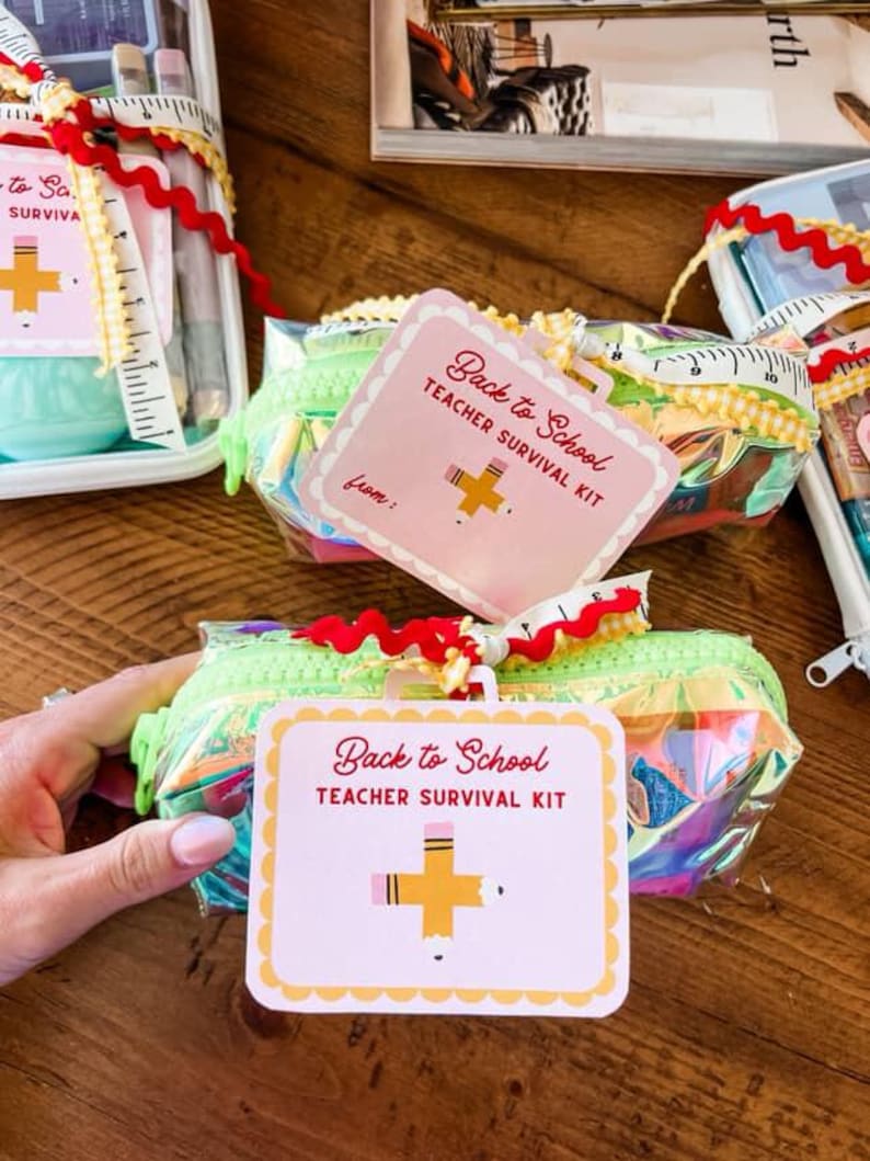 K&ouml;nnte beinhalten: Eine transparente, schillernde Federtasche mit einem gr&uuml;nen Rei&szlig;verschluss und einem Etikett mit der Aufschrift "Back to School Teacher Survival Kit". Das Etikett zeigt eine Bleistiftgrafik. Die Tasche ist mit roten und gelben B&auml;ndern verziert.