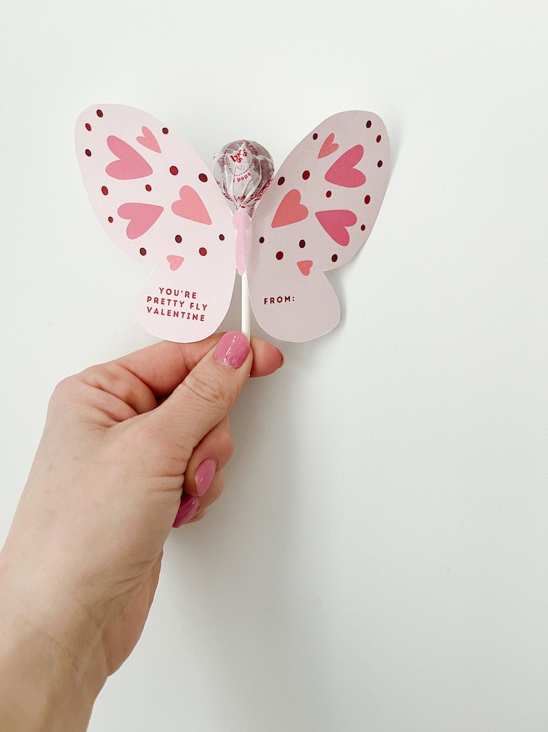 May include: Pink butterfly shaped lollipop with the text 'You're Pretty Fly Valentine' and 'From:' on the wings.