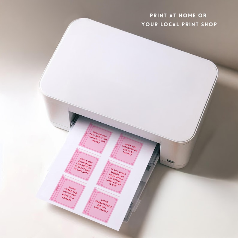 Pode incluir: Uma impressora branca est&aacute; imprimindo uma folha de papel com cart&otilde;es rosa em forma de livro. Cada cart&atilde;o tem uma pergunta sobre livros. O texto "PRINT AT HOME OR YOUR LOCAL PRINT SHOP" est&aacute; no topo.