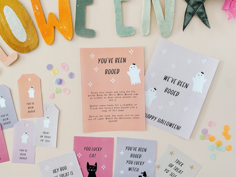 May include: A collection of Halloween-themed cards and tags with ghost illustrations and the phrase "You've Been Booed." The cards are in pink, purple, and gray, with confetti scattered around. The tags say "Treat or Treat Yo' Self."