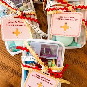 K&ouml;nnte beinhalten: Transparente Plastiktaschen gef&uuml;llt mit verschiedenen Artikeln, gebunden mit einem wei&szlig;en und gelben Ma&szlig;band und rotem Zickzackband. Jede Tasche hat ein rosa Etikett mit der Aufschrift "Back to School Teacher Survival Kit" mit einem Bleistift- und Kreuzdesign.