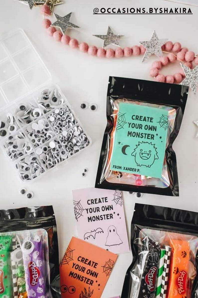Puede incluir: Una colecci&oacute;n de kits de manualidades con tem&aacute;tica de Halloween. La imagen presenta recipientes de pl&aacute;stico transparente llenos de ojos saltones, bolsas negras con tarjetas de "Crea tu propio monstruo" y Play-Doh. Estrellas decorativas y una guirnalda rosa en el fondo.