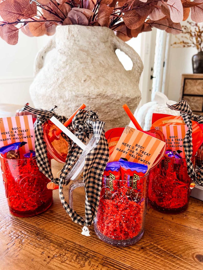 May include: Red glass mugs filled with candy and red paper shred. Each mug has a straw, a black and white checkered ribbon, and a small card that reads "BOO! HERE'S A TREAT FOR YOU HAPPY HALLOWEEN".