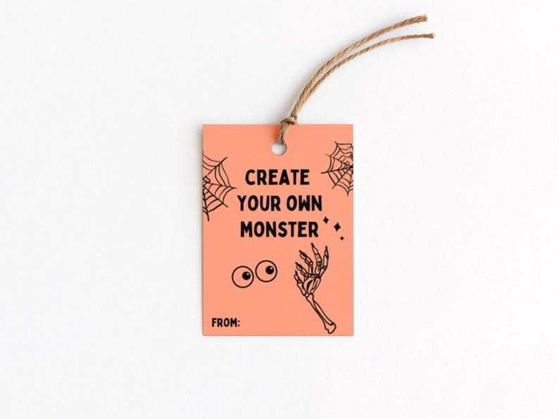 Puede incluir: Una etiqueta de regalo de color melocot&oacute;n con el texto "CREATE YOUR OWN MONSTER" en negro. La etiqueta presenta una telara&ntilde;a, ojos saltones y un dibujo de una mano de esqueleto. Una cuerda marr&oacute;n est&aacute; atada en la parte superior.