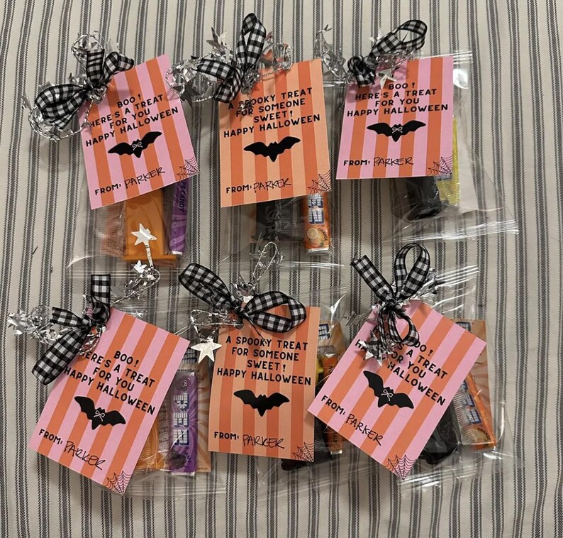 May include: Halloween treat bags with pink and orange striped tags that read "Boo! Here's a treat for you Happy Halloween" and "A spooky treat for someone sweet! Happy Halloween." Each bag is tied with a black and white checkered ribbon.