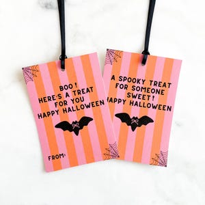 May include: Two Halloween gift tags with black ribbons. The tags have pink and orange stripes, with a black bat and spiderweb design. Text on the tags reads "BOO! Here's a treat for you Happy Halloween" and "A spooky treat for someone sweet! Happy Halloween."