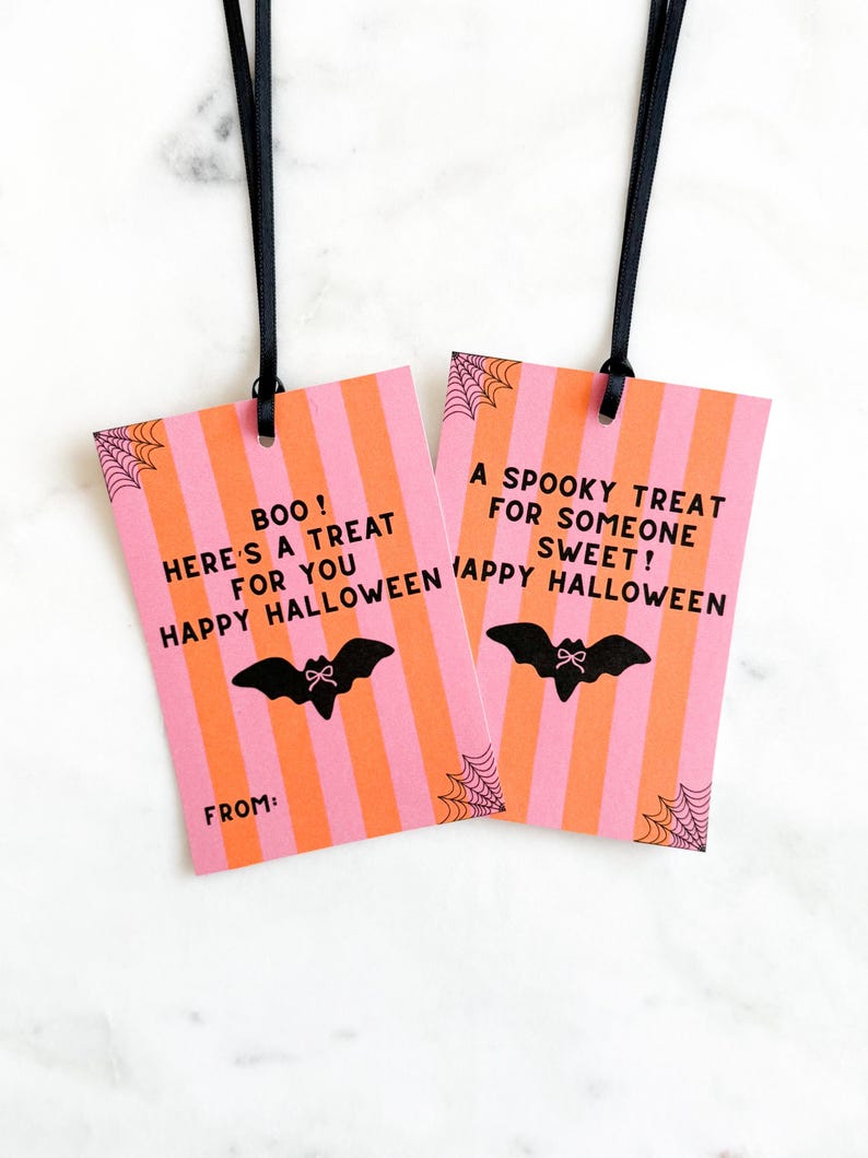 May include: Two Halloween gift tags with black ribbons. The tags have pink and orange stripes, with a black bat and spiderweb design. Text on the tags reads "BOO! Here's a treat for you Happy Halloween" and "A spooky treat for someone sweet! Happy Halloween."