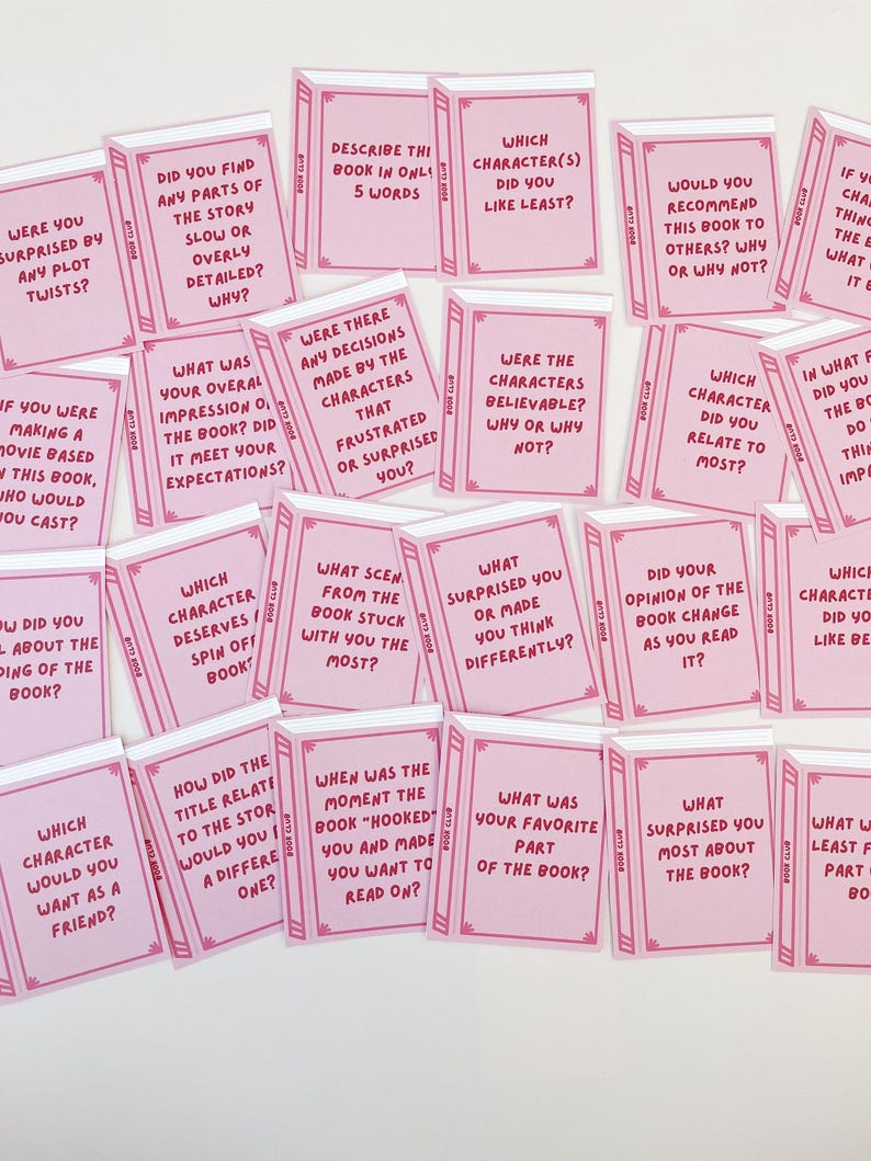 Pode incluir: Cart&otilde;es cor-de-rosa para um clube de leitura, dispostos de forma aleat&oacute;ria. Cada cart&atilde;o, em forma de pequeno livro, apresenta perguntas como &laquo;Qual personagem voc&ecirc; menos gostou?&raquo; e &laquo;O que mais te surpreendeu?&raquo; em texto branco.