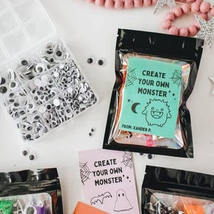 Puede incluir: Una colecci&oacute;n de kits de manualidades con tem&aacute;tica de Halloween. La imagen presenta recipientes de pl&aacute;stico transparente llenos de ojos saltones, junto con bolsas negras que contienen Play-Doh y tarjetas que dicen "Crea tu propio monstruo".