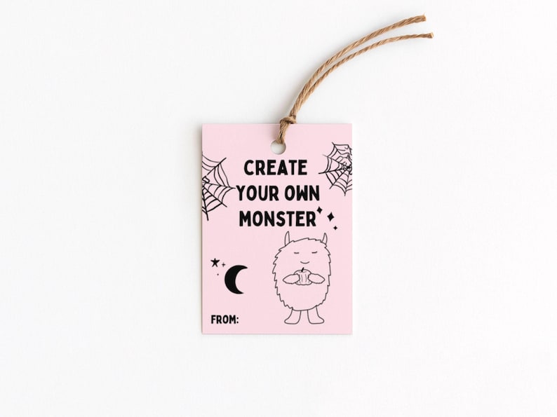 Puede incluir: Una etiqueta de regalo rosa con el texto "CREATE YOUR OWN MONSTER" en negro. La etiqueta presenta un monstruo de dibujos animados, telara&ntilde;as, una luna creciente y estrellas. Una cuerda marr&oacute;n est&aacute; atada en la parte superior.