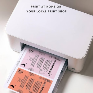 May include: A white printer is shown printing pink and orange Halloween-themed cards. The cards have black illustrations of ghosts, spiders, and pumpkins. Text on the cards reads "YOU'VE BEEN BOOED" and "PRINT AT HOME OR YOUR LOCAL PRINT SHOP."