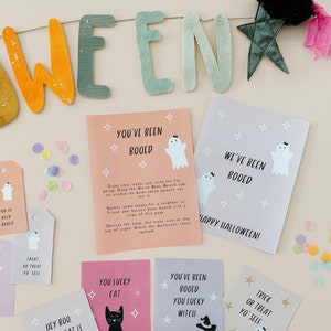 May include: A Halloween-themed display featuring a banner that spells out "WEEN" in orange and green letters. Several cards and tags with ghost and star graphics are scattered around, with phrases like "You've Been Booed" and "Trick or Treat Yo' Self".