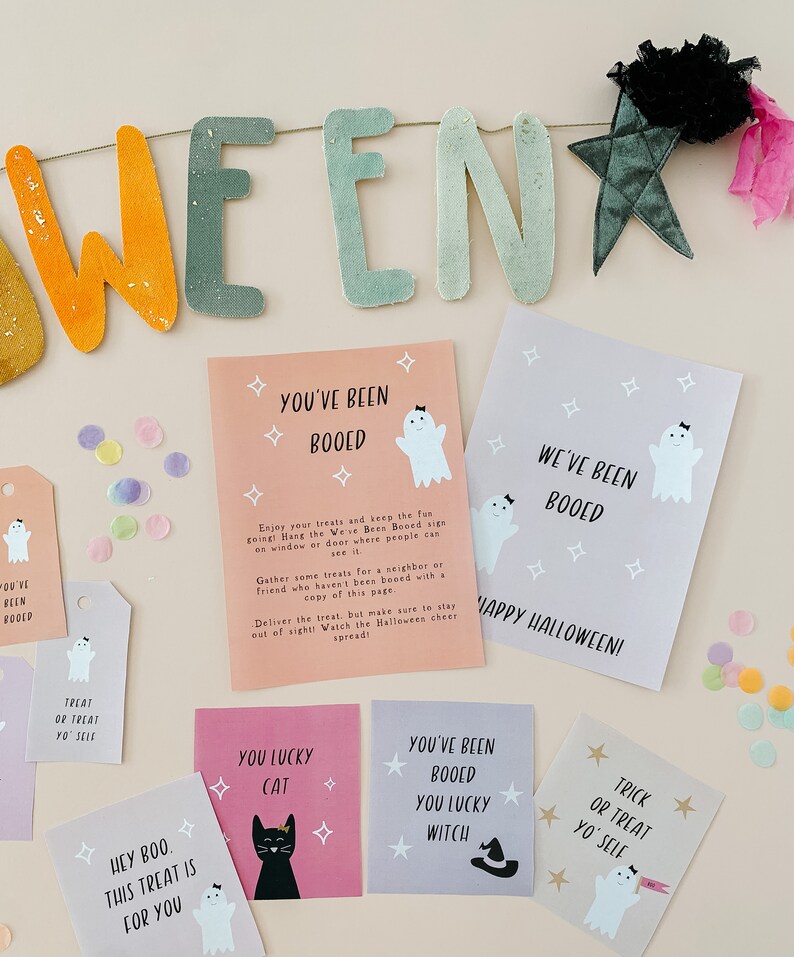 May include: A Halloween-themed display featuring a banner that spells out "WEEN" in orange and green letters. Several cards and tags with ghost and star graphics are scattered around, with phrases like "You've Been Booed" and "Trick or Treat Yo' Self".