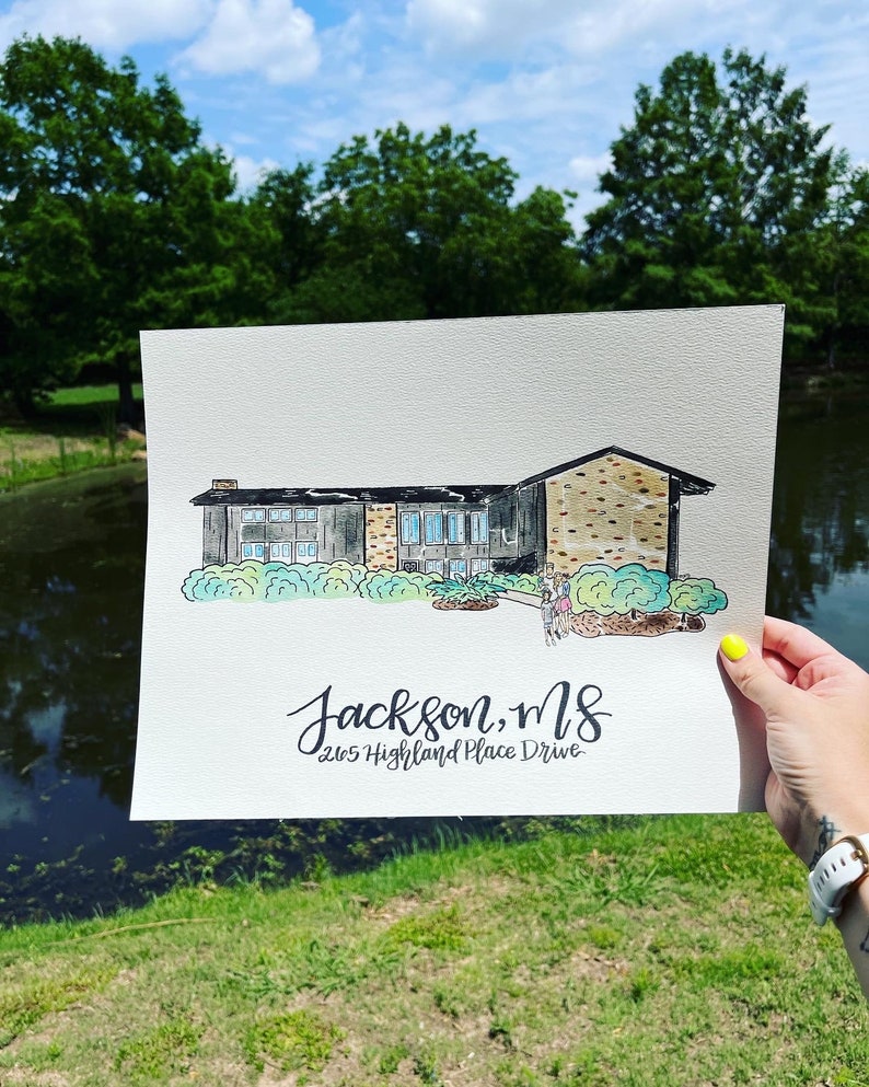 Puede incluir: Pintura a la acuarela de una casa con el texto "Jackson, MS 2615 Highland Place Drive". La casa tiene un tejado negro, ladrillo y revestimiento gris, y ventanas te&ntilde;idas de azul. La pintura se sostiene frente a un estanque y &aacute;rboles.
