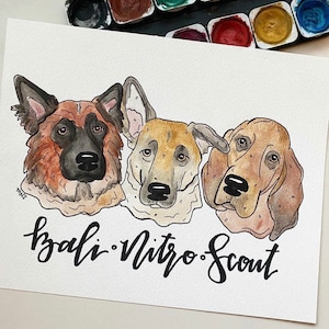 May include: Watercolor painting of three dogs: a German Shepherd, a mixed breed, and a Basset Hound. The names "Bali, Nitro, Scout" are written in cursive below the portraits. A watercolor paint set is in the background.