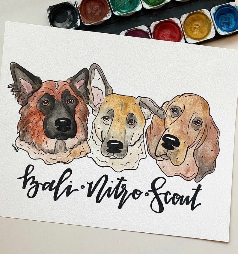 May include: Watercolor painting of three dogs: a German Shepherd, a mixed breed, and a Basset Hound. The names "Bali, Nitro, Scout" are written in cursive below the portraits. A watercolor paint set is in the background.