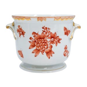 May include: White ceramic planter with red floral and butterfly designs. The planter has a gold rim and handles. The floral design includes a large peony and smaller flower clusters. The planter sits on a small pedestal base.