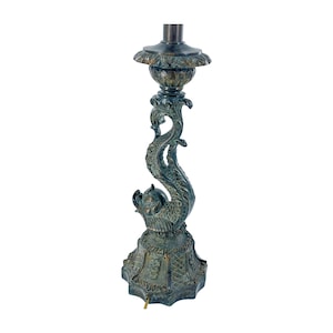 May include: An antique bronze-colored lamp base with a detailed dolphin design. The base features a decorative floral top, a curved dolphin body, and an ornate base. The lamp base is a vintage piece, perfect for adding a touch of elegance to any room.