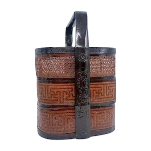 May include: A three-tiered, woven bamboo basket with a dark brown handle and accents. The basket features intricate geometric patterns and a dark, decorative band around the top and bottom. The handle is dark brown with floral carvings.