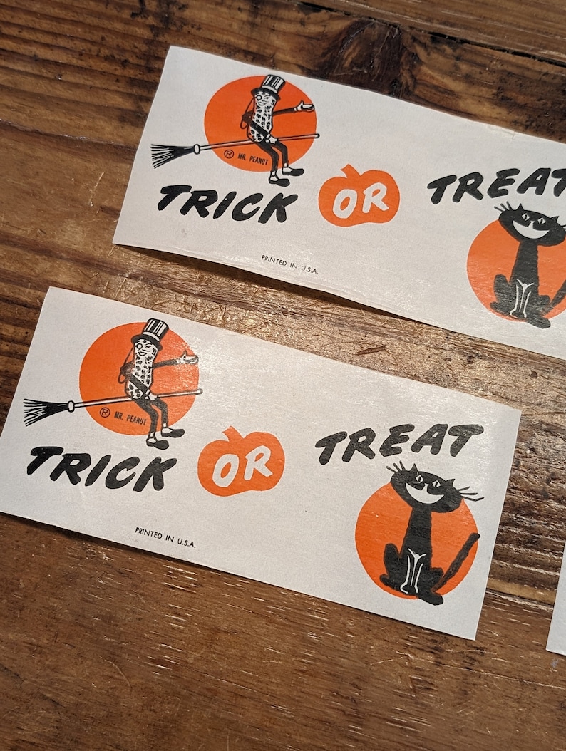 K&ouml;nnte beinhalten: Halloween-Aufkleber mit Mr. Peanut auf einem Besen, einem K&uuml;rbis und einer schwarzen Katze. Die Worte "Trick or Treat" sind in Schwarz gedruckt. Gedruckt in den USA.