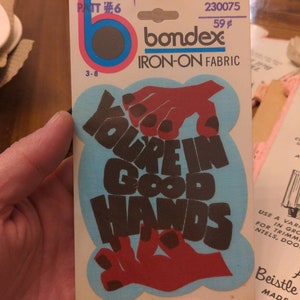 Puede incluir: Parche de tela termoadhesiva con el texto "You're in good hands" en letras negras sobre un fondo azul. Dos manos rojas con uñas negras se muestran en el parche. El parche está empaquetado en una tarjeta blanca con el nombre de la marca "bondex" y el precio "59¢".