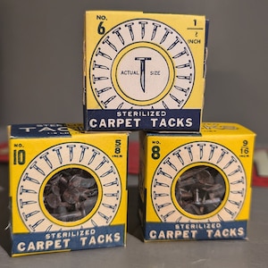 May include: Three boxes of sterilized carpet tacks. The boxes are yellow with black lettering and feature a picture of the tacks. The boxes are labeled with the size of the tacks: 1/2 inch, 5/8 inch, and 9/16 inch.