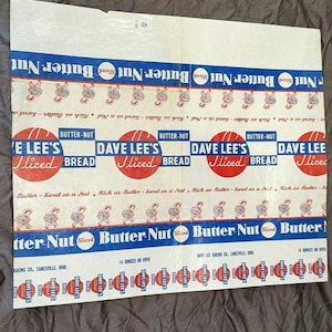 May include: Vintage Dave Lee's Butter Nut Sliced Bread packaging. The design features a repeating pattern of the brand name in blue and red, with a cartoon peanut character. The packaging is cream-coloured with text.