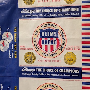 May include: A vintage white paper bag with a red, white, and blue design. The bag features the text "Always the Choice of Champions" and "Olympic Helms Bread." The bag is decorated with a red, white, and blue circle logo with the text "Olympic Helms Bread." The bag also features a smaller circle logo with the text "Gold Medal Winner."
