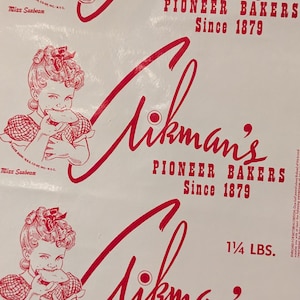 Op de afbeelding: Een vintage advertentie voor Mikman's Pioneer Bakers, met een rode en witte illustratie van een meisje dat een sandwich eet. De tekst luidt "Mikman's Pioneer Bakers Since 1879" en "1 1/4 LBS."