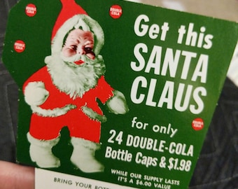 Könnte beinhalten: Eine grüne Werbekarte mit einer Abbildung des Weihnachtsmanns im roten Anzug. Der Text lautet: Get this SANTA CLAUS for only 24 DOUBLE-COLA Bottle Caps & $1.98. WHILE OUR SUPPLY LASTS IT'S A $6.00 VALUE. BRING YOUR BOTTLE CAPS TO DOUBLE-COLA.