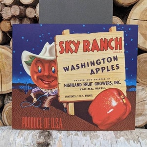 May include: A vintage illustration of a cartoon apple wearing a cowboy hat and holding a lasso. The apple is standing in front of a wooden sign that reads "Sky Ranch Brand Washington Apples". The sign also includes the text "Packed and Shipped by Highland Fruit Growers, Inc. Yakima, Wash. Contents: 1 U.S. Bushel". The background is a dark blue sky with white stars.