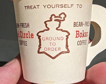 May include: A white paper coffee cup with a red and brown logo that says "Treat Yourself To Bean-Fresh Circle Coffee Ground To Order Bean-Fresh Bokar Coffee".