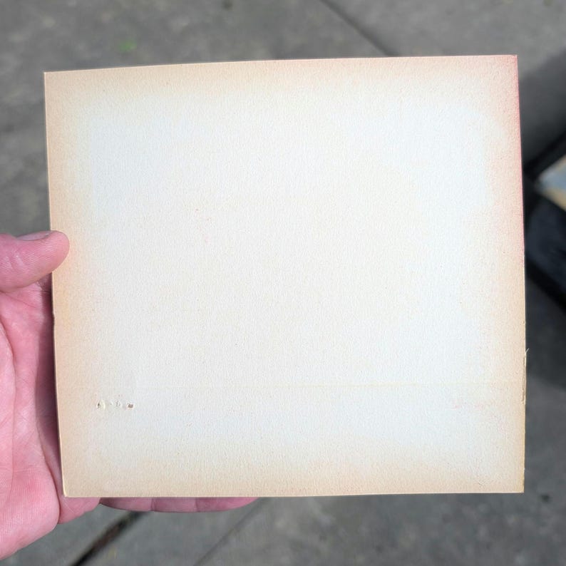 K&ouml;nnte beinhalten: Ein rechteckiges St&uuml;ck gealtertes Papier mit einem cremefarbenen Mittelteil und einem verblassten, hellbraunen Rand. Das Papier wird von einer Hand gehalten, und die Kanten weisen leichte Abnutzungserscheinungen auf.