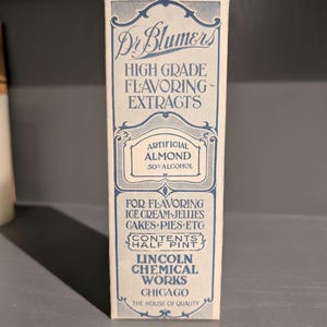 May include: A vintage box of Dr. Blumers High Grade Flavoring Extracts, featuring a blue and white label with the text "Artificial Almond 50% Alcohol". The box is labeled for flavoring ice cream, jellies, cakes, pies, and other foods. It is a half pint size and made by Lincoln Chemical Works in Chicago.
