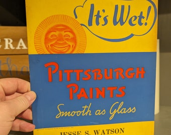 Op de afbeelding: Een vintage advertentie voor Pittsburgh Paints, met een lachende zon met de tekst "It's Wet!" en de slogan "Smooth as Glass". De advertentie bevat de contactgegevens van het bedrijf: Jesse S. Watson, 26 Summit Avenue, Ashley, Delaware, Telefoon: 2-3979.
