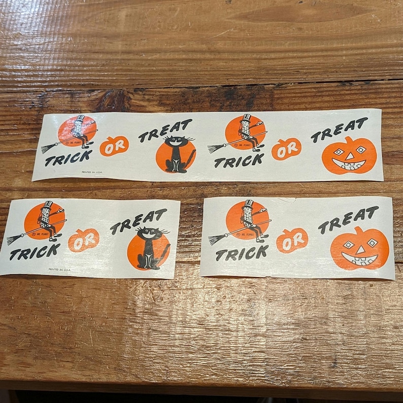 K&ouml;nnte beinhalten: Drei Vintage-Papierstreifen zum Thema Halloween mit orangefarbenen und schwarzen Grafiken. Jeder Streifen zeigt eine Hexe auf einem Besen, eine schwarze Katze und einen K&uuml;rbis, zusammen mit den Worten "Trick or Treat."