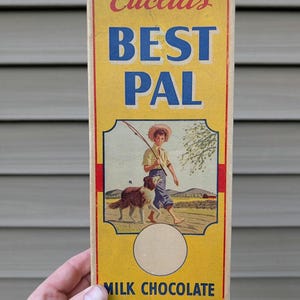 Puede incluir: Embalaje vintage de barra de coco y chocolate con leche Euclid's Best Pal. La caja amarilla presenta un niño con un perro y el texto "BEST PAL" en azul. La parte superior de la caja dice "Euclid's" en escritura roja.