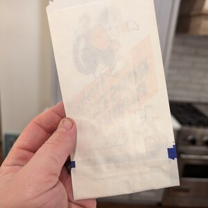Peut inclure: Un sac en papier blanc avec une bande bleue le long du bord inf&eacute;rieur. Le sac a une image fan&eacute;e d'un personnage de dessin anim&eacute; sur le devant. Le texte sur le sac indique "Joyeux anniversaire".