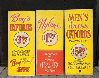 May include: Three vintage yellow and red signs advertising shoes. The signs advertise "Boy's Oxfords", "Nylons $1.07", and "Men's Dress Oxfords".